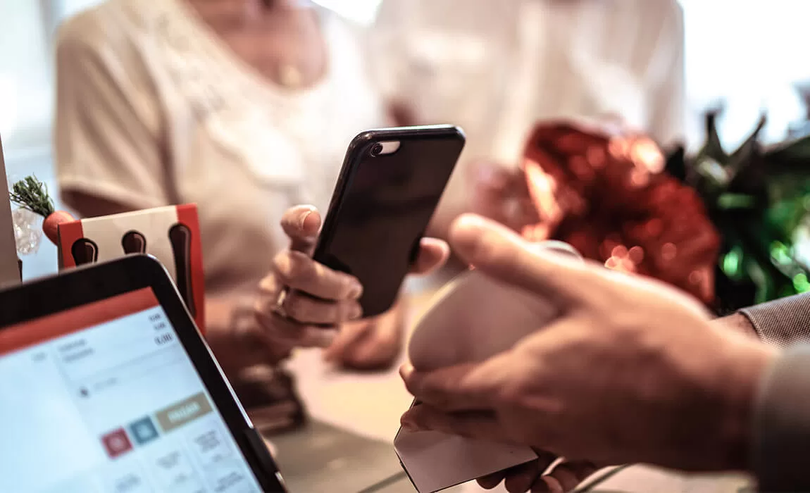 Hand holding a phone up to a payment device, showing the mobile payment options available with NMI.