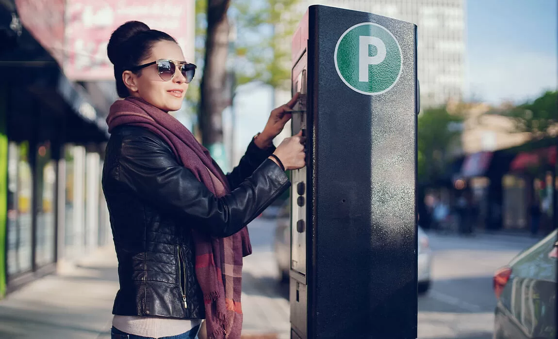 A woman standing outside, inserting her credit card into an unattended payment machine in a parking lot.