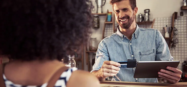 A worker using a digital tablet and payment device to complete a credit card transaction for the customer across the counter.