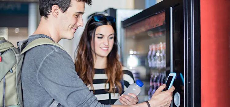 A man holding up a mobile device to an unattended payment vending machine.