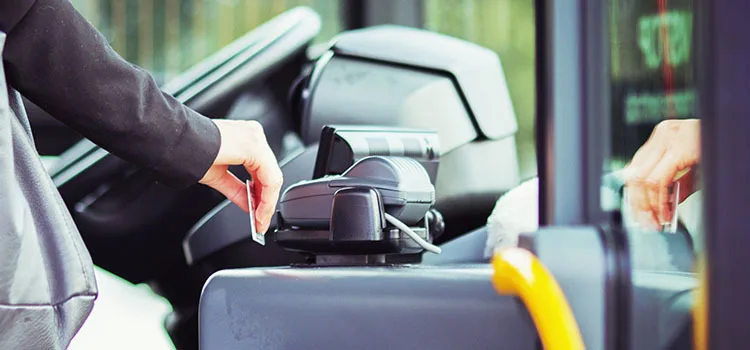 An arm swiping a credit card on a payment device at the entrance of a bus.