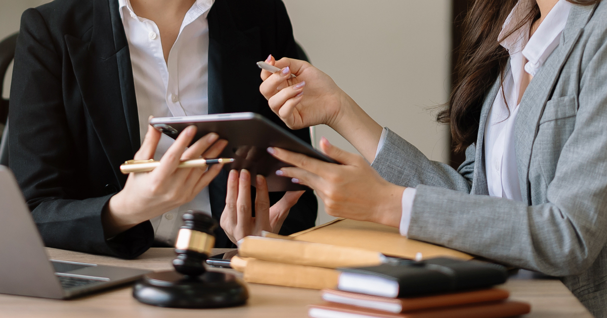 Two business professionals reviewing information on a tablet in an office setting, surrounded by legal and financial icons, representing Visa VAMP fraud and compliance guidance