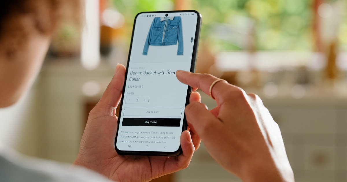 Person using a smartphone to shop online for a denim jacket, illustrating the concept of AI-powered agentic commerce and autonomous digital payments.