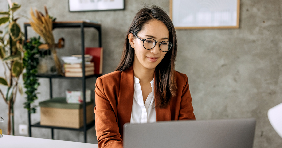 A professional woman working at her laptop in a modern office, representing the payments industry's shift toward more realistic AI expectations and the rise of seamless, software-led merchant onboarding.