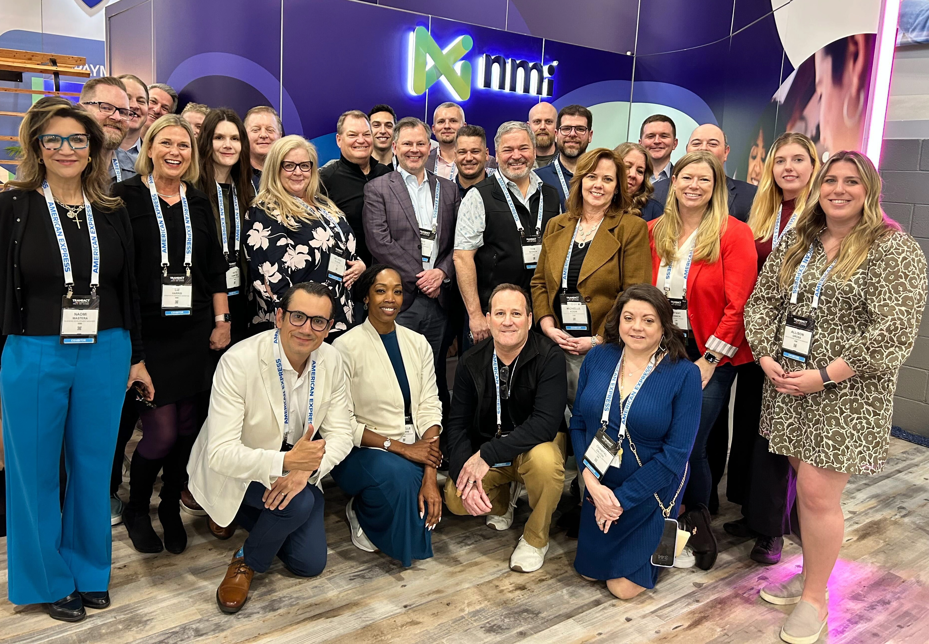 The NMI te stand together at an exhibition looking proud in front of the NMI branded booth