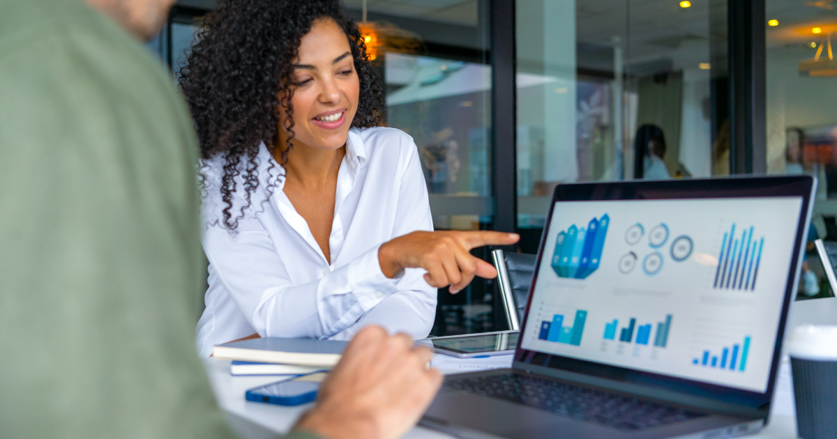 Merchant is sat near her computer with colleagues and points to a graph on the screen.