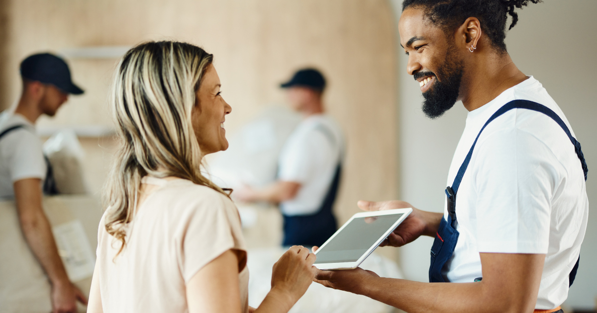 A decorator smiles as he hands over his ipad to allow the customer to pay. She smiles back.