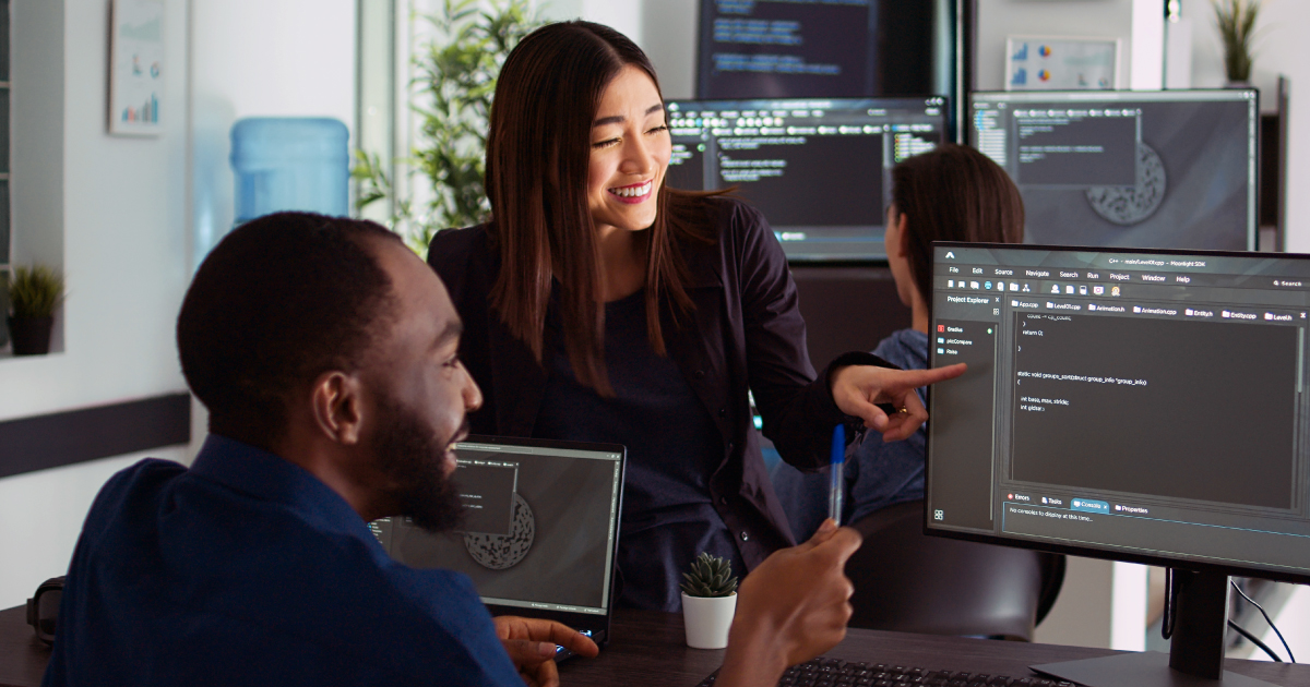 Two office workers smile at a computer in a modern setting