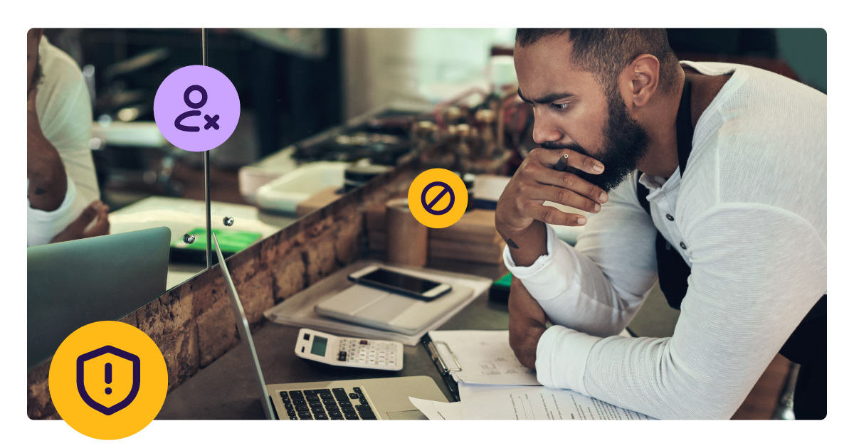 A small business owner sits at his counter, leaning over a laptop with a concerned expression, representing the financial threat that payment fraud poses to merchants