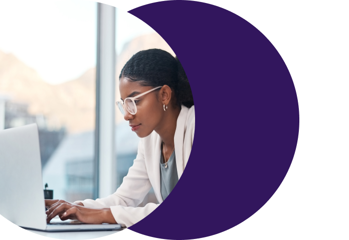 Woman in glasses focused on a laptop in a warehouse or operations setting, representing a payments professional using Merchant Central's automated ticket routing and workflow tools to handle merchant support requests more efficiently.