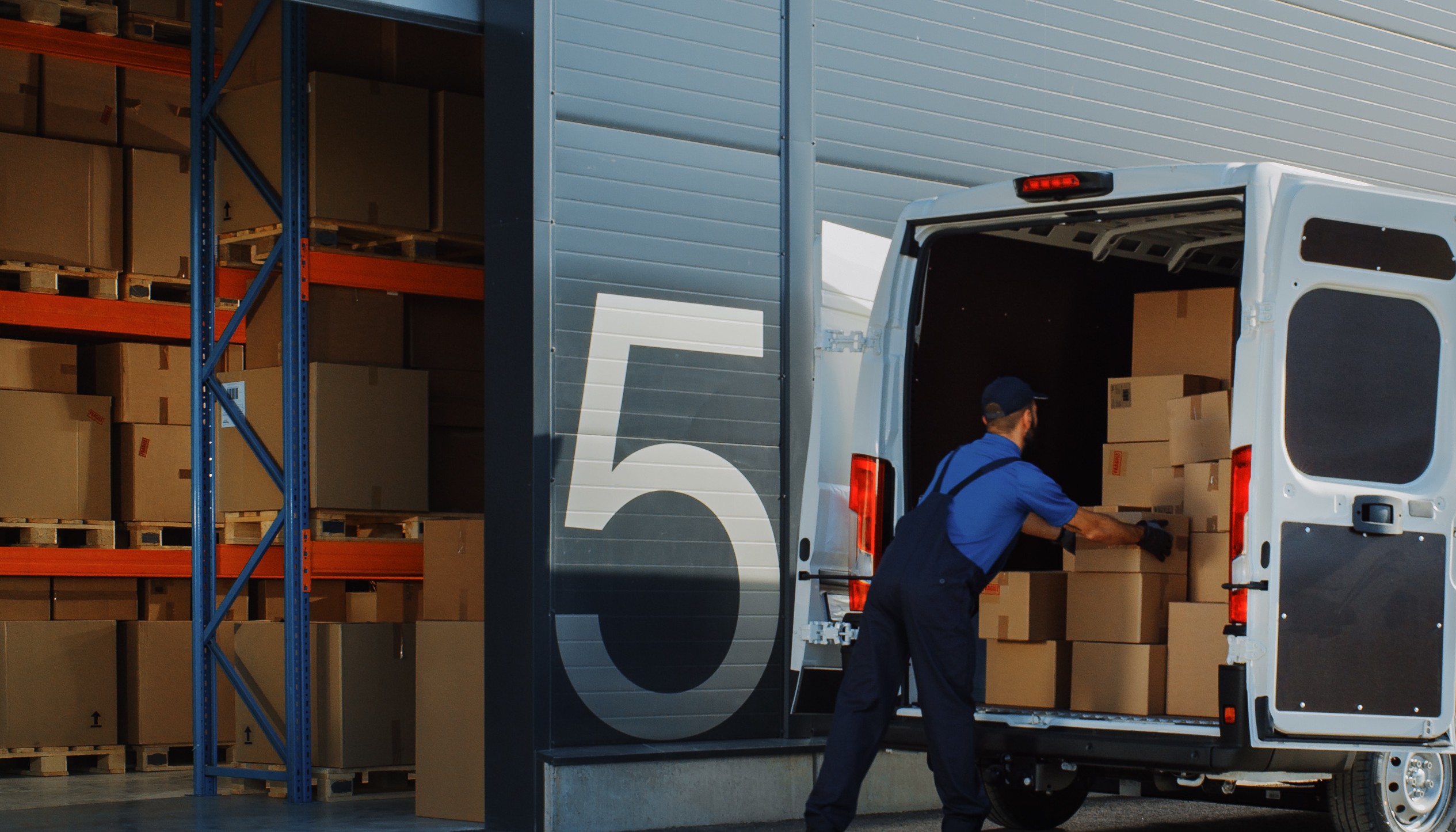 Warehouse workers loading cardboard boxes into a white delivery van at a fulfillment center loading dock, representing the surge in ecommerce order volume during Amazon Prime Day 2026.