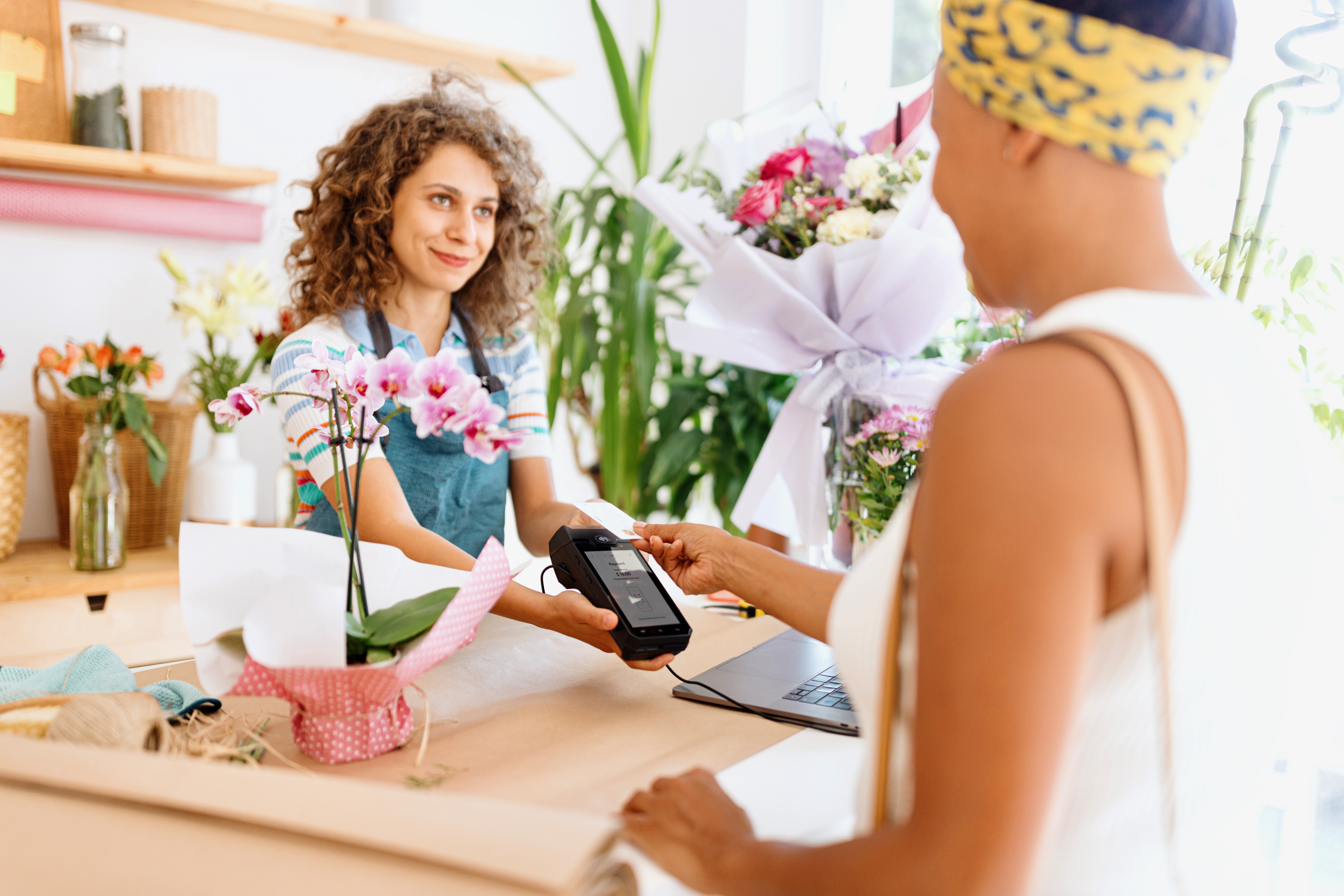 A florist takes a contactless card payment on a handheld smart POS terminal in a flower shop