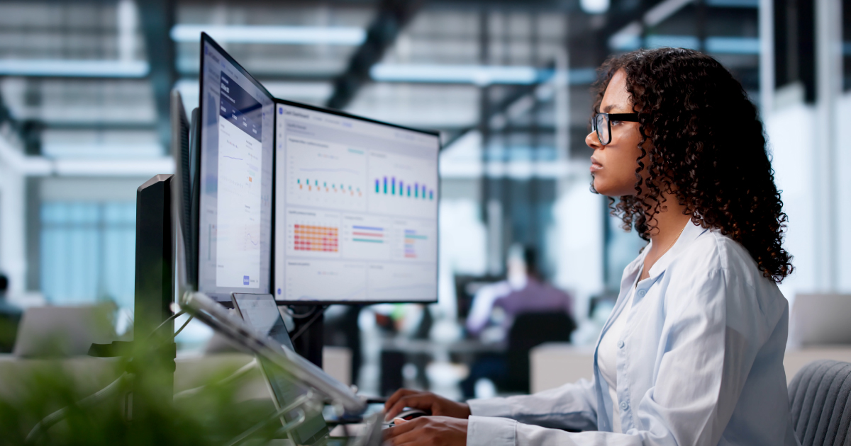 Payments professional reviews merchant data dashboards on dual monitors, with icons for reporting, gateways and connected tools