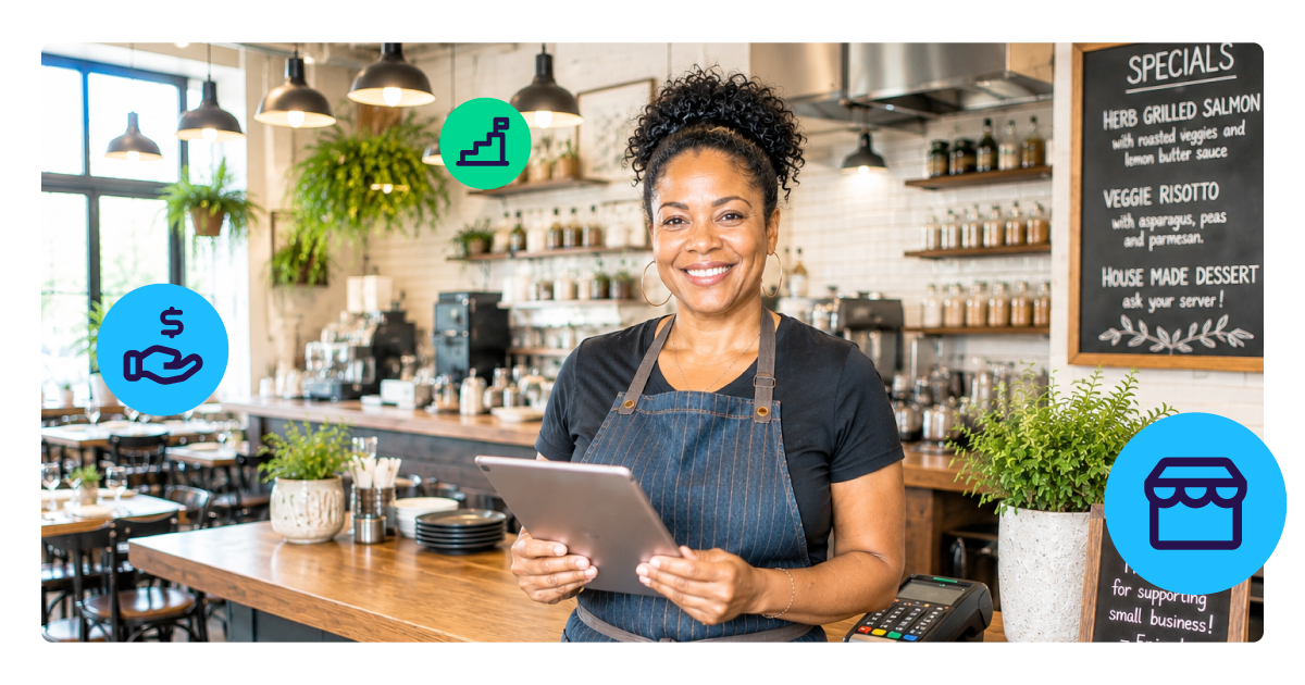 Smiling restaurant owner in a denim apron holds a tablet behind the counter of her café, a card terminal beside her.