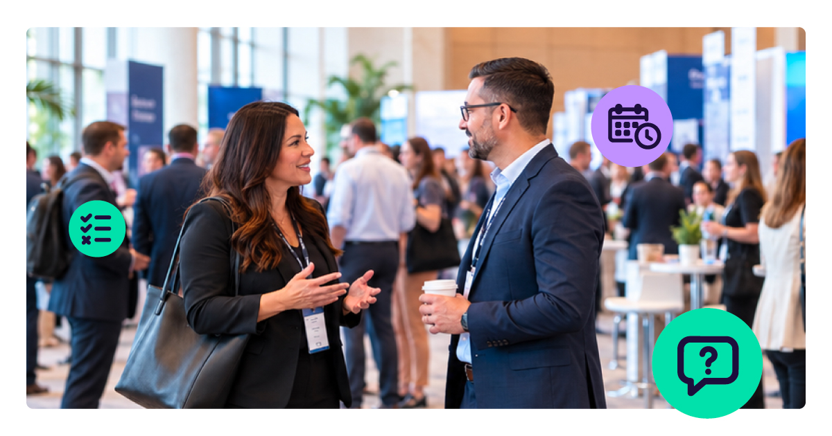 Two professionals wearing conference badges talk on a busy trade show floor, one gesturing as she speaks while the other listens holding a coffee.